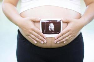 pregnant woman and her husband hand splice hugging the tummy Heart shaped show love for the unborn baby in the belly relaxing at home in bedroom. wait birth date expecting a baby stand in the outdoors photo