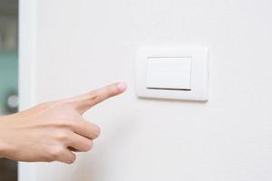 Turn off the light, close up finger man hand is closing the power switch with wall at home  to save energy. reduce global warming. photo