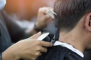 corte de pelo de hombre de persona que se afeita el cabello con estilo, con cortapelos de peluquero peluquero con las manos en la barbería. tono vintage de relleno y enfoque suave selectivo. foto