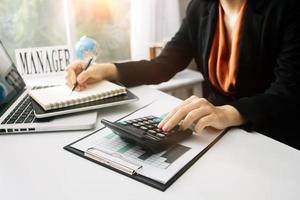 mujer empresaria usando una calculadora con un bolígrafo en la mano, calculando los gastos financieros en la oficina del hogar foto