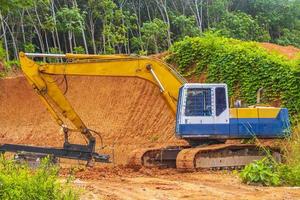 Big yellow excavator digs destroys forest jungle on Phuket Thailand. photo