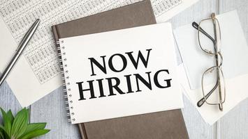 On the table charts, calculator and notebook with the Now Hiring text photo