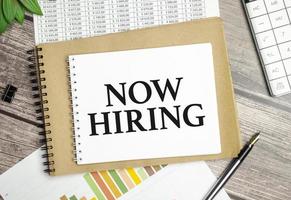 On the table charts, calculator and notebook with the Now Hiring text photo