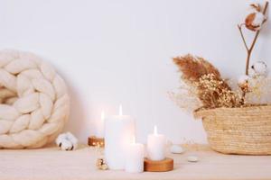 Home decoration with candles, basket and flowers over white wall. Interior design concept. Close up, copy space photo