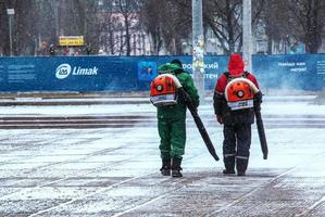 Dnepropetrovsk, Ukraine - 02.04.2022 Seasonal work of city utilities in the park. A worker with a motorized backpack blower blows snow from a park path. photo