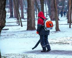 Dnepropetrovsk, Ukraine - 02.04.2022 Seasonal work of city utilities in the park. A worker with a motorized backpack blower blows snow from a park path. photo