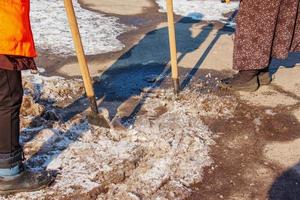 una trabajadora limpia el hielo y quita la nieve de las losas de pavimentación con un rompehielos. foto