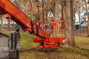 Dnepropetrovsk, Ukraine - 11.22.2021 A mobile crane with an orange color basket is used in a public park to trim trees. photo