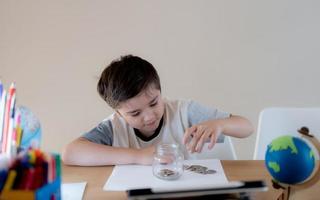 niño de la escuela poniendo monedas de dinero en un frasco transparente, niño contando su dinero ahorrado, niño sosteniendo monedas en sus manos, niños aprendiendo a ahorrar para el concepto futuro foto