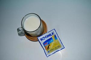 BLITAR, INDONESIA - October 3rd 2022 Glass of white milk and Indomilk white creamer in sachet isolated on white background photo