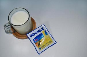 BLITAR, INDONESIA - October 3rd 2022 Top view Glass of white milk and Indomilk white creamer in sachet isolated on white background. Copy space object photo