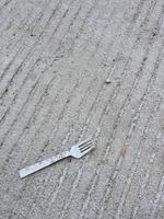 A plastic fork litter on top of a concrete road. Ab photo