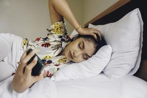 una joven atractiva se queda dormida mientras sostiene su teléfono en la cama. foto