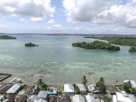 Aerial view of village near beautiful beach with small island in the background in Maluku, Indonesia photo