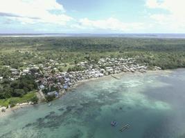 Aerial view of village near beautiful beach with small island in the background in Maluku, Indonesia photo