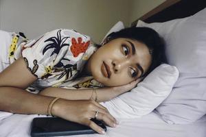una joven triste frunciendo el ceño desde la cama esperando una llamada mientras sostenía el smartphone. foto