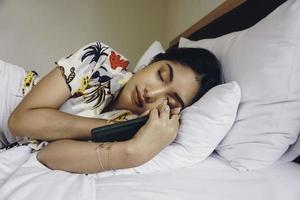 An attractive young woman falls asleep while holding her handphone on the bed. photo