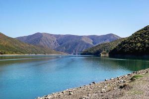 Scenic view on bank of lake with blue water and mountains in sunny weather. Caucasus Mountains, Georgia. photo