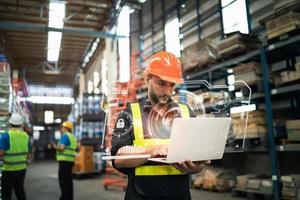 Professional manager man employee using laptop check stock working at warehouse. Worker wearing high visibility clothing and a hard hat, helmet and checking and count up goods or boxes for delivery. photo