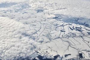 Aerial view over clouds top to snow covered rivers, fields and roads, winter fresh frosty air