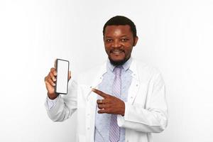 Smiling black doctor man with small beard in white coat holds smartphone blank mockup photo