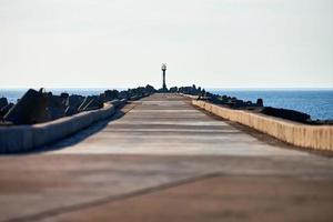 Empty long concrete pier with breakwaters and signal lighthouse in European port, copy space photo