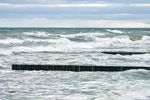 View of blue sea with foaming waves and wooden breakwaters photo