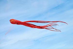 Bright red pink octopus kite flying in blue sky with clouds, red octopus-shaped kite, kite festival photo