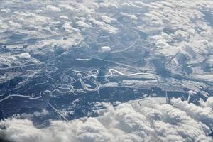 vista aérea del paisaje nublado sobre las nubes hasta ríos, carreteras, ciudades y campos cubiertos de nieve, aire invernal foto