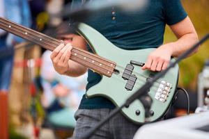 Hands of bassist playing green bass electric guitar on concert stage, musician playing bass guitar photo