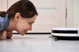 Friendly cheerful woman looking at robotic vacuum cleaner. photo