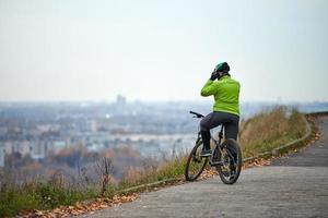 ciclista en la cima de la colina mirando el paisaje urbano, vista trasera, espacio de copia foto