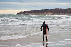 Male surfer in swim suit walking along sea with surfboard photo