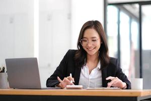 Beautiful Asian businesswoman analyzes charts using laptop calculator at the office. photo