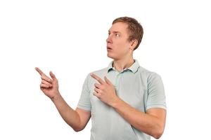 Surprised man with funny face in grey T-shirt pointing finger to left, white background photo