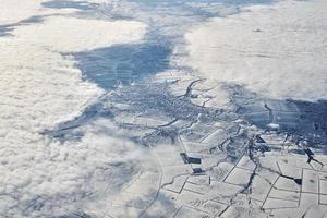 Aerial cloudscape view over clouds top to snow covered rivers, roads, cities and fields, winter air photo