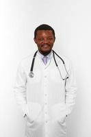 Sonriente médico barbudo negro hombre en bata blanca con estetoscopio aislado sobre fondo blanco. foto