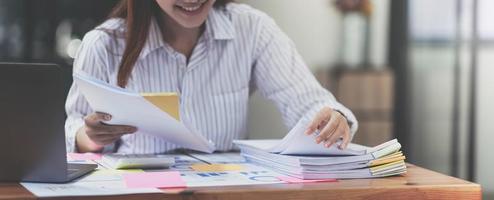 Business Documents concept  Employee woman hands working in Stacks paper files for searching and checking unfinished document achieves on folders papers at busy work desk office. Soft focus photo