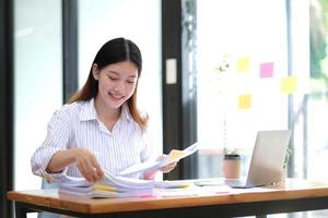 Business Documents concept  Employee woman hands working in Stacks paper files for searching and checking unfinished document achieves on folders papers at busy work desk office. Soft focus photo