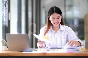 Business Documents concept  Employee woman hands working in Stacks paper files for searching and checking unfinished document achieves on folders papers at busy work desk office. Soft focus photo