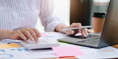 Businesswoman press the white calculator to calculate the numbers in the company financial documents, the finance department prepares the document and forwards it to be checked before the meeting. photo