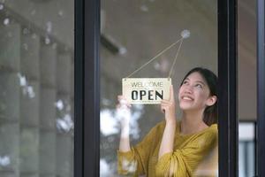 Small business owner smiling while turning the sign for the opening of the place after the quarantine due to covid-19. Close up of woman hands holding sign now we are open support local business. photo