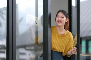 Young Asia manager girl changing a sign from closed to open sign on door cafe looking outside waiting for clients after lockdown. Owner small business, food and drink, business reopen again concept photo