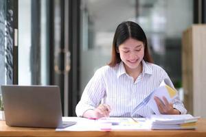 Pretty Asian woman sitting in the office, calculator, working on data, charts and documents on the table in business workspace. photo