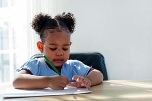 los niños africanos dibujan y hacen sus deberes en el aula. una niña disfruta aprendiendo y jugando con dibujos en papel. foto