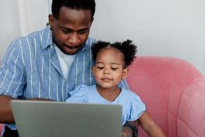 African father and little daughter wearing blue shirts using laptop online shopping on sofa. photo