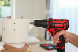 man assembling white table furniture at home using cordless screwdriver photo