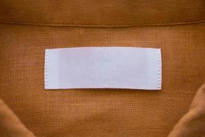 White blank clothing tag label on brown linen shirt fabric texture background photo