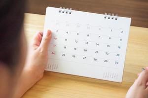 página del calendario con mano femenina sosteniendo un bolígrafo en la mesa del escritorio foto