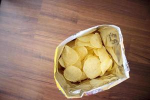 Patatas fritas en una bolsa de aperitivos abierta de cerca en el suelo de la mesa foto